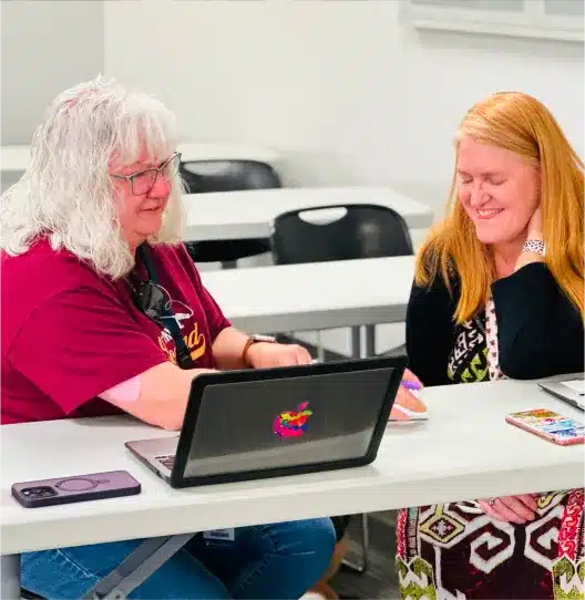 Two women smiling while looking at a laptop together at a table