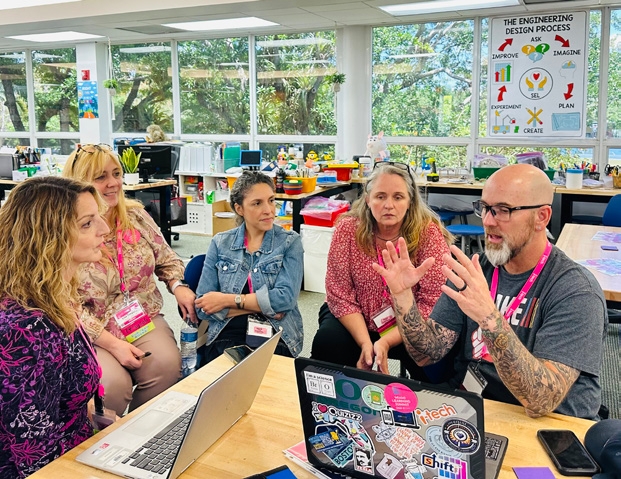 i-Tech team member discussing technology with educators gathered around a laptop in a classroom